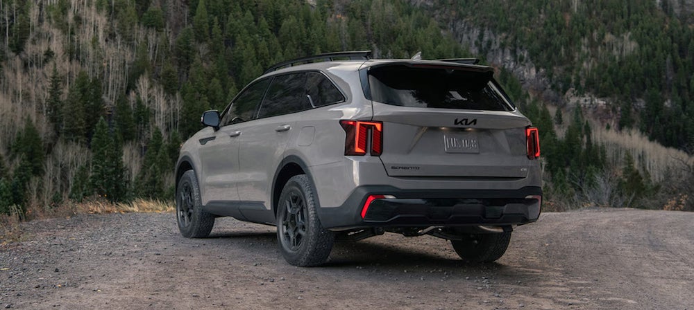 The side and back of a gray 2026 Kia Sorento SUV, parked in front of a wooded mountainside