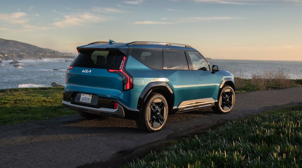 A bright blue Kia EV9 SUV driving along the coastline