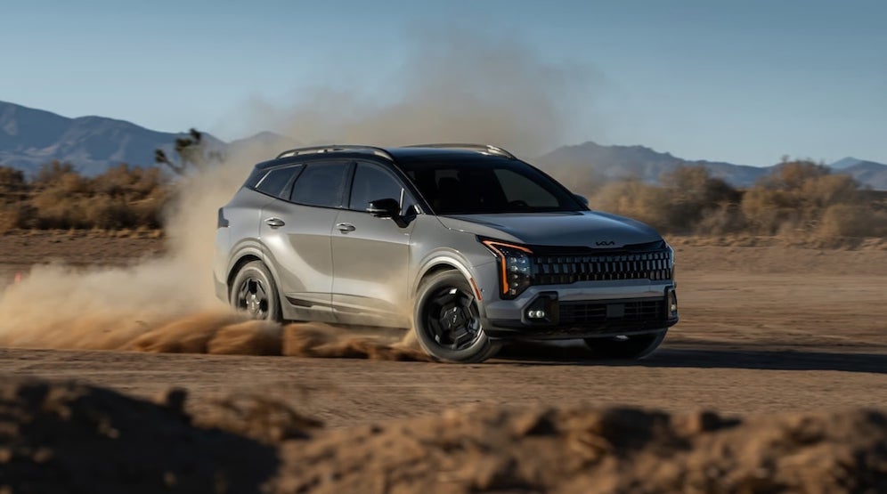 A gray 2026 Kia Sportage SUV driving in the desert, with dust flying up from its wheels