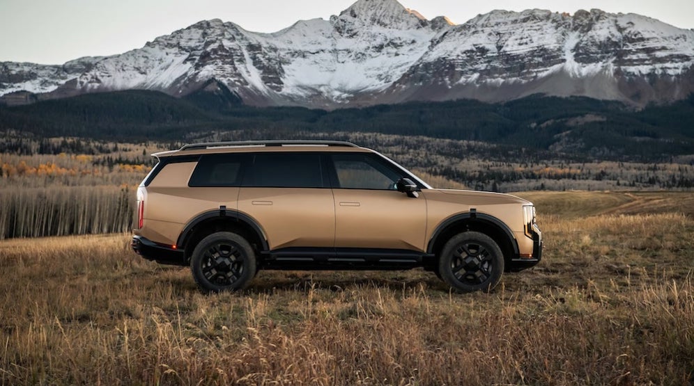 A brown 2027 Kia Telluride SUV parked in a field with mountains in the background