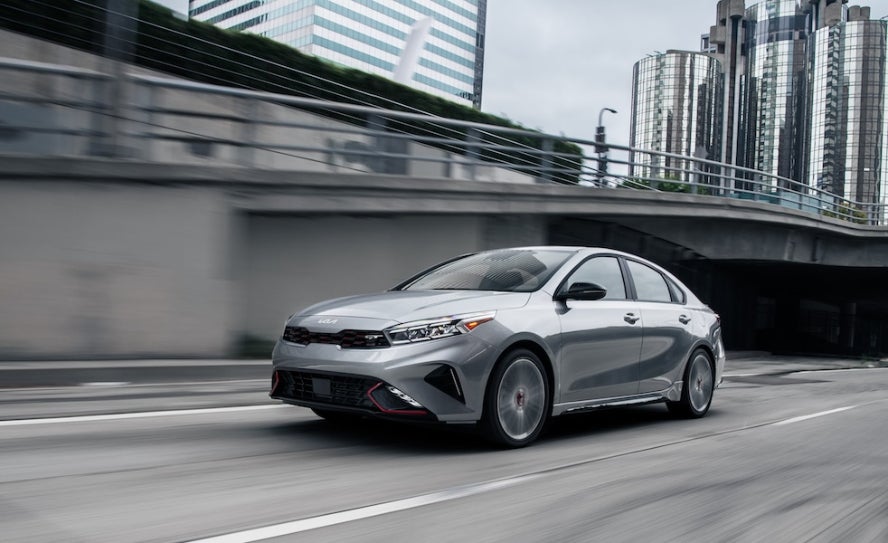 A silver 2024 Kia Forte driving down a city highway