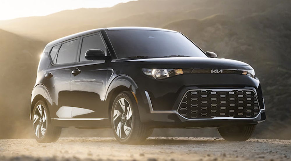 A black 2026 Kia Soul on a dusty gravel road, with mountains in the background