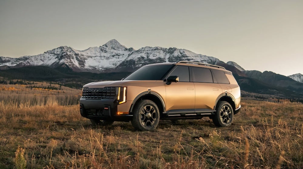A brown 2027 Kia Telluride SUV parked in a field with mountains in the distance