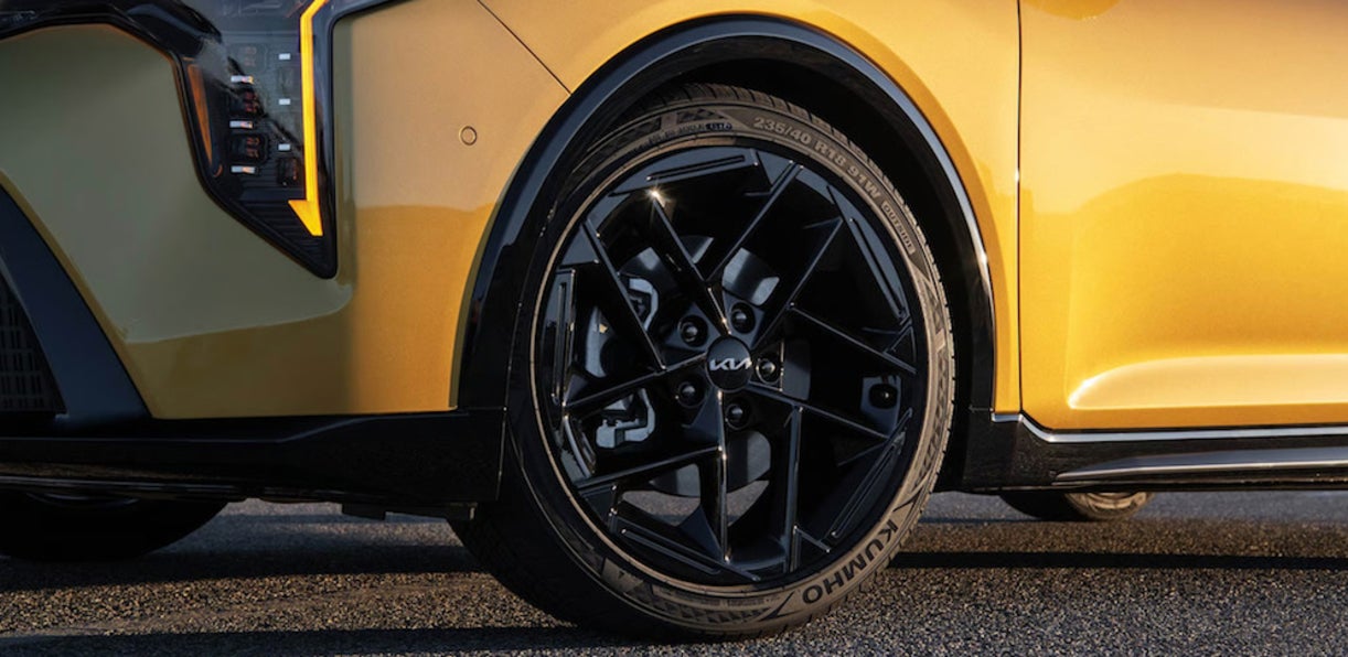 A closeup of the headlight and tire of an orange Kia K4 hatchback