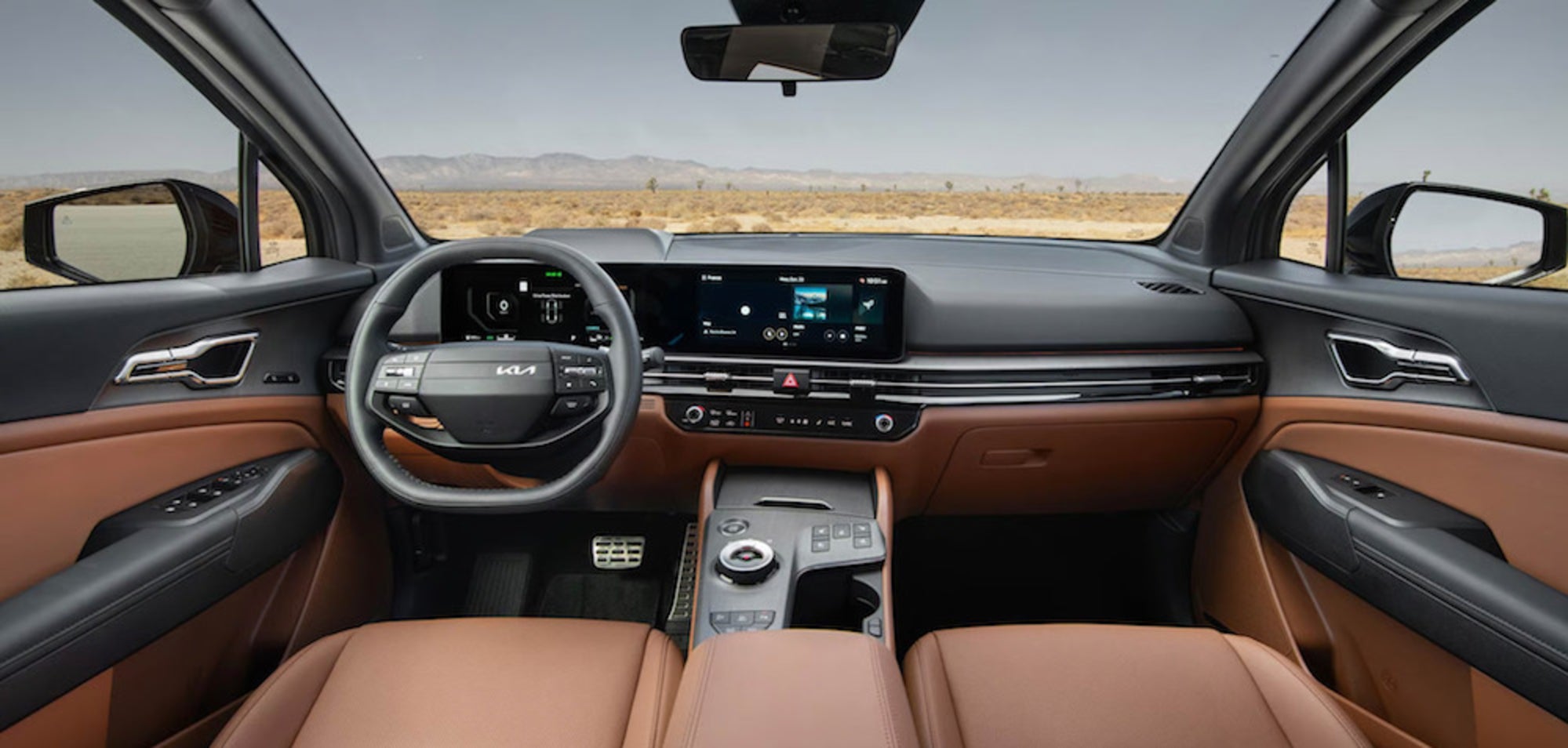 The front seats and dashboard of the 2026 Kia Sportage SUV, featuring brown upholstery and a view of the desert through the windshield