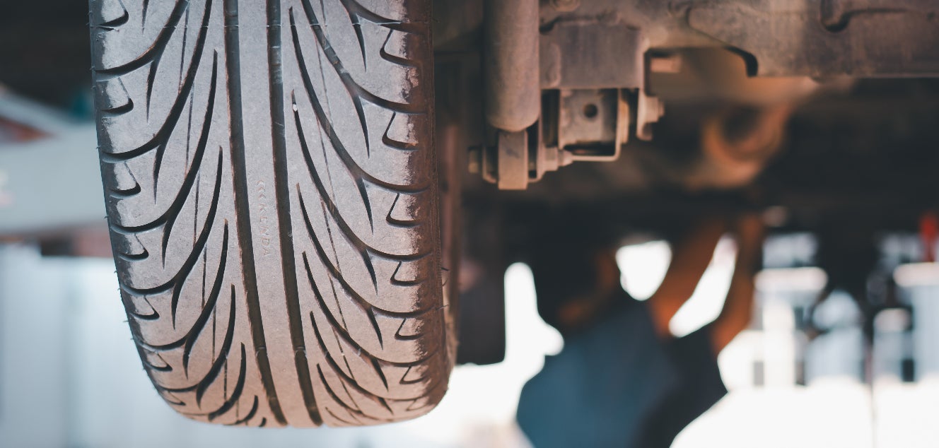 A closeup of a vehicle’s wheel on a car, while a technician works on the car’s undercarriage