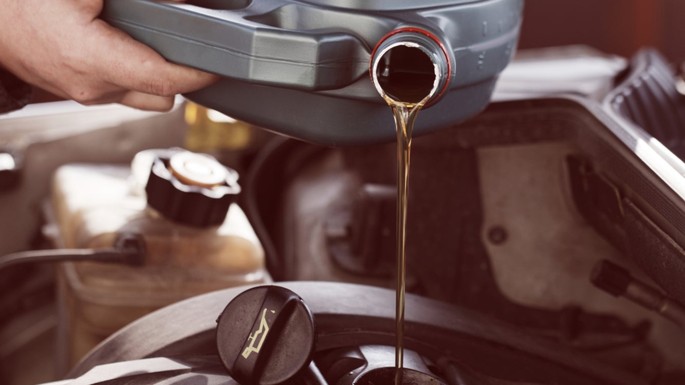 A white person’s hand pouring a bottle of oil into a car engine