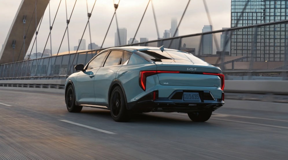 A light blue 2025 Kia K4 sedan driving over a bridge