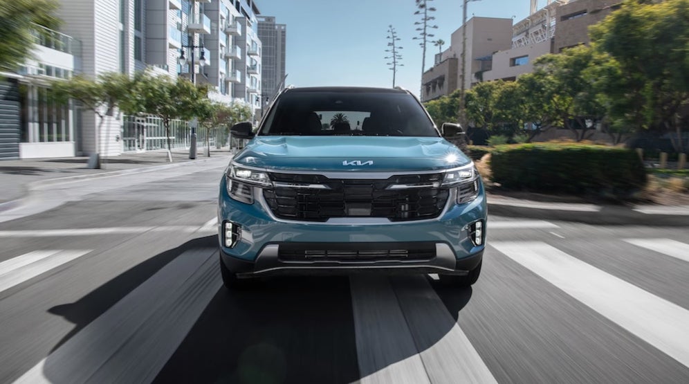 A blue 2026 Kia Seltos SUV driving down a city street